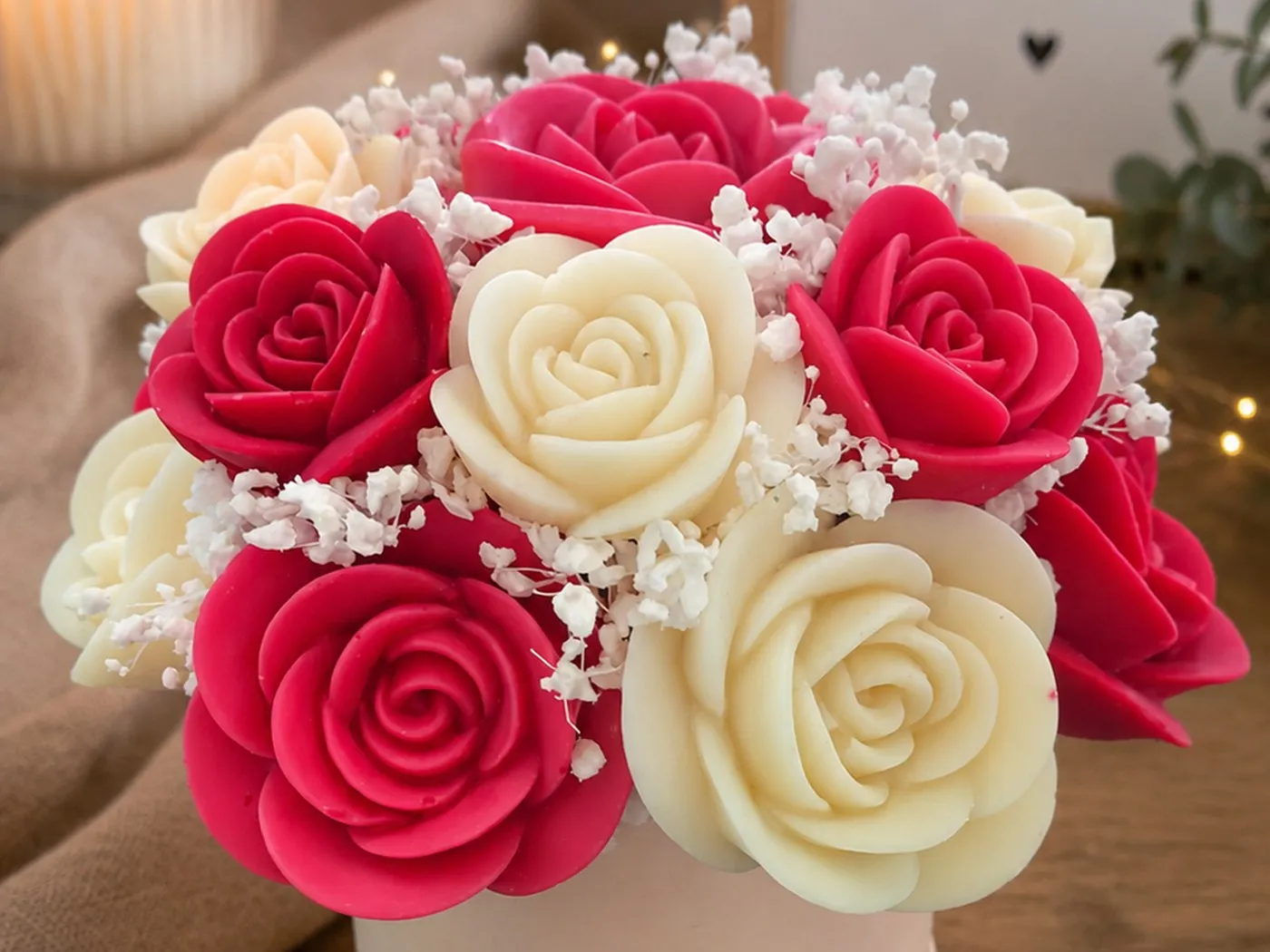 Bouquet rond de roses de cire rouges et ivoire dans une boîte ronde blanche, bougie allumée en arrière-plan