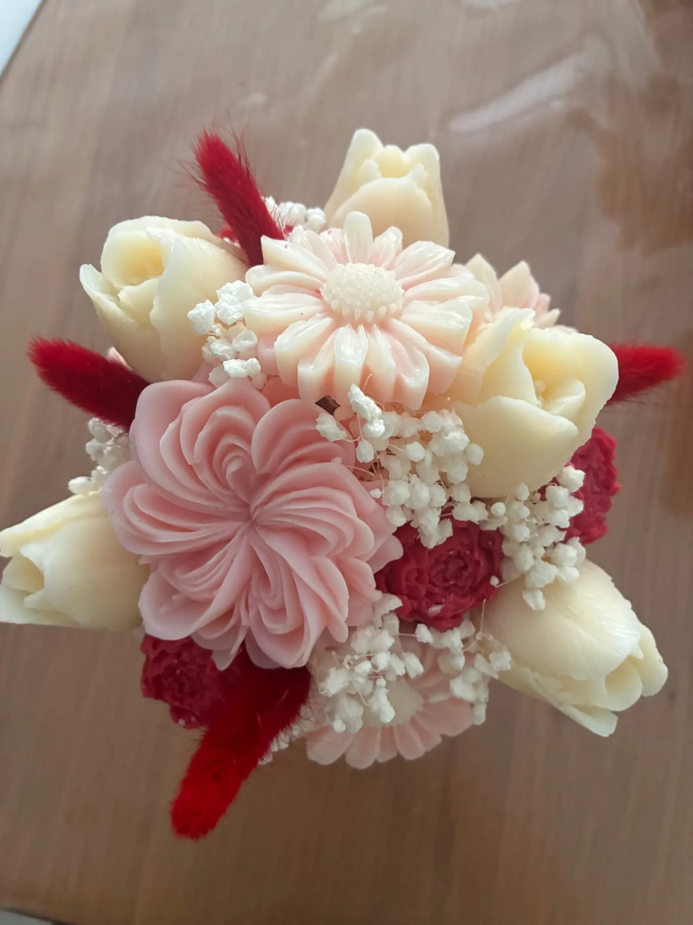 Bouquet rond de fleurs de cire en camaïeu rose, rouge et blanc, sur une table en bois