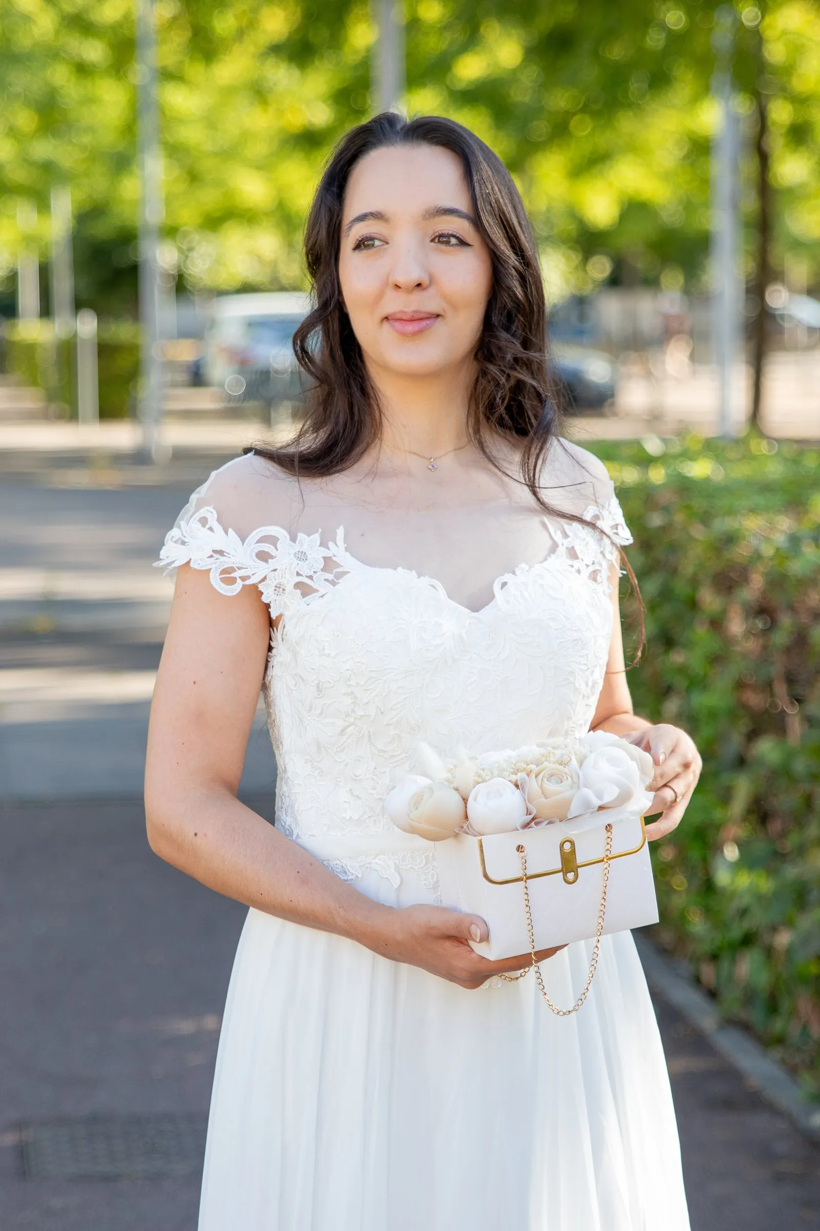 Robe de mariée bustier en dentelle illusion, portrait avec pochette fleurie, en extérieur